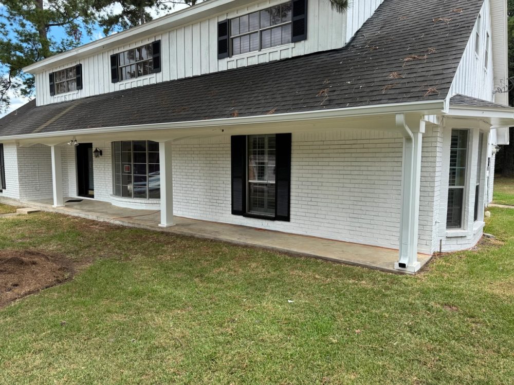 White seamless gutter and matching downspout across the covered front porch of a white-painted brick home