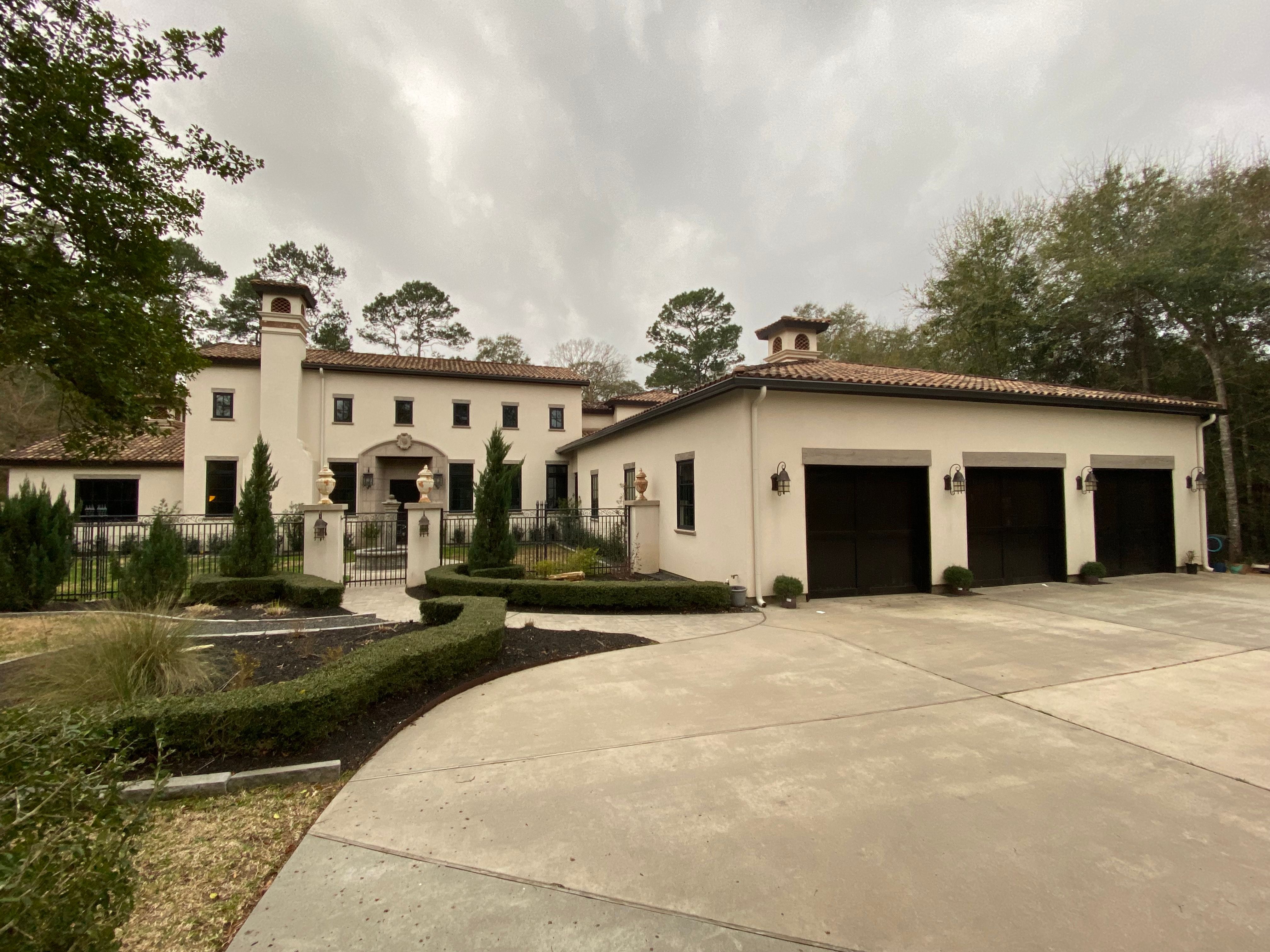 Brown seamless gutters and cream round downspouts on a stucco Conroe home with a three-bay garage and terracotta tile roof