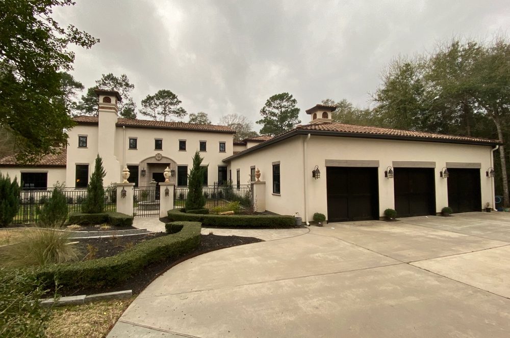 Brown seamless gutters and cream round downspouts on a stucco Conroe home with a three-bay garage and terracotta tile roof