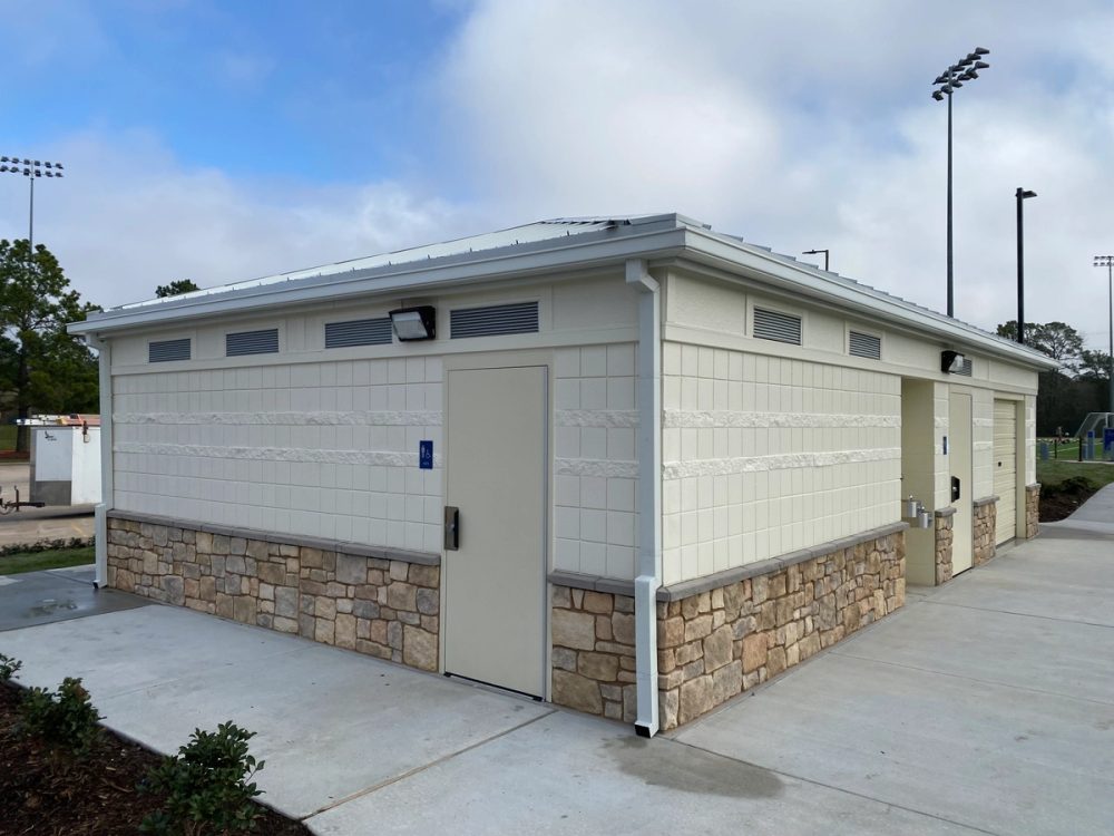 White box gutters and smooth downspouts on a white block park building with stone skirting
