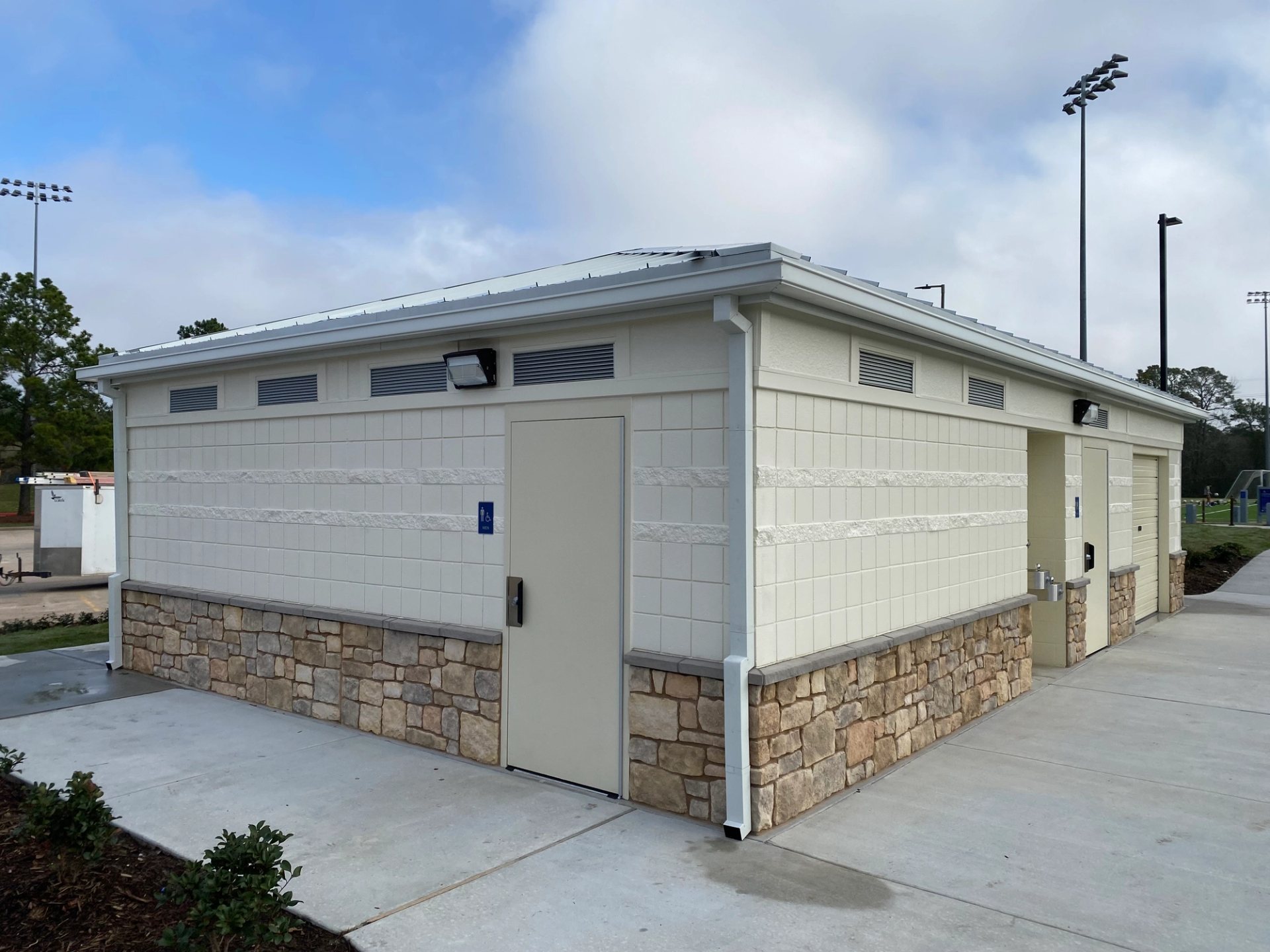 White box gutters and smooth downspouts on a white block park building with stone skirting