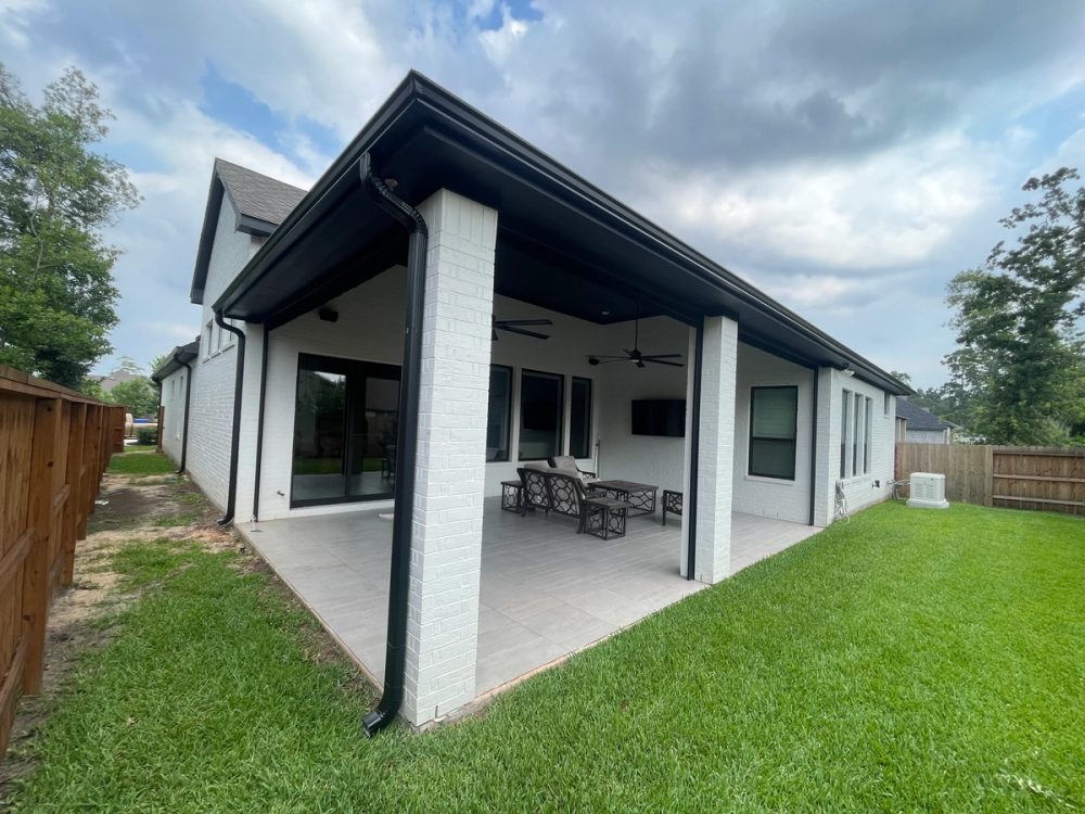 Black seamless gutters and matching downspouts around a white-brick covered patio in Conroe