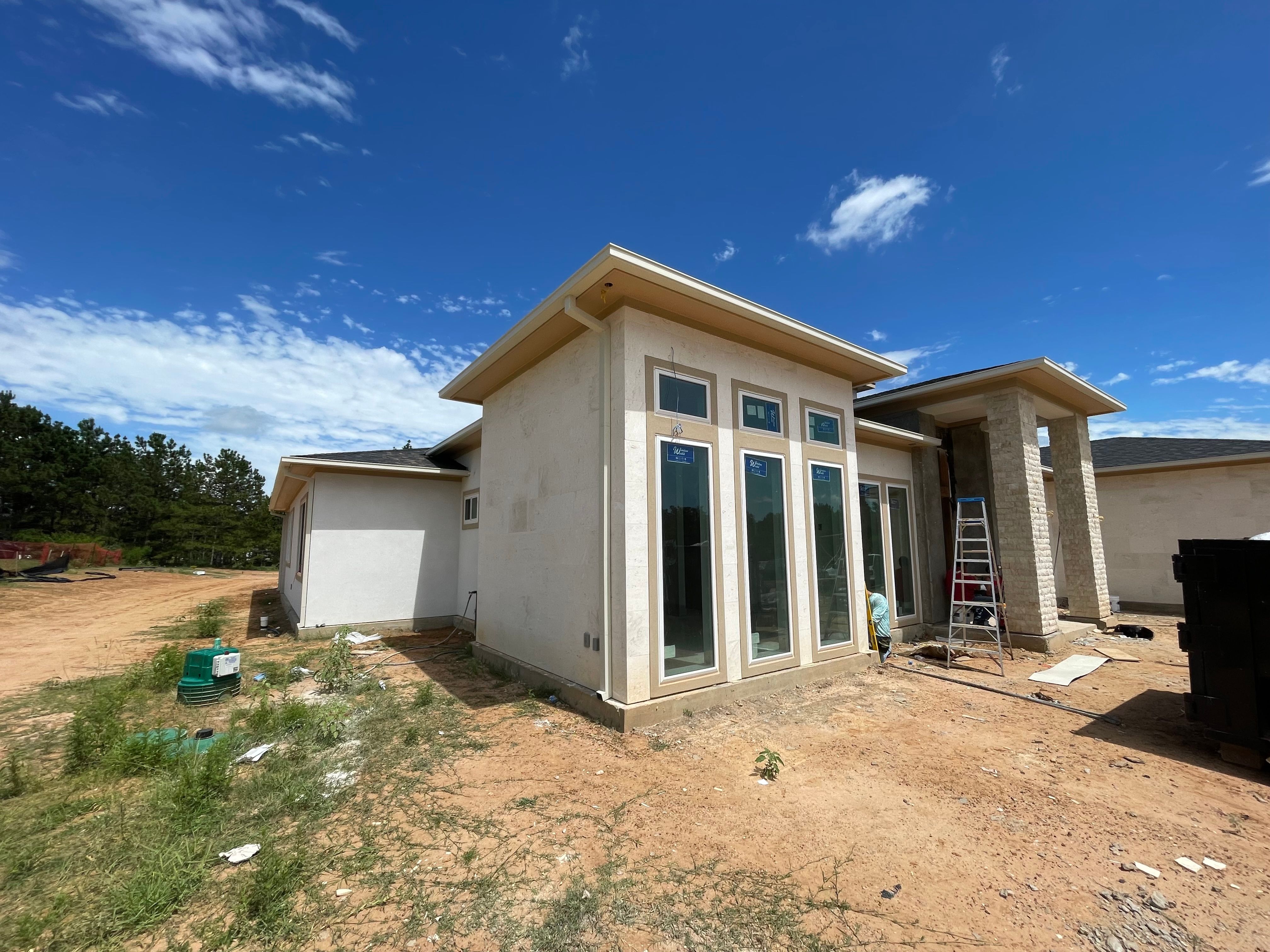 Almond box gutters and downspout above tall windows on a Montgomery stucco-and-stone home