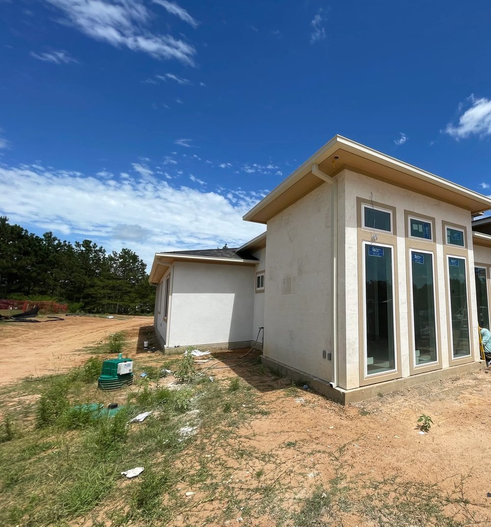 Almond box gutters and downspout above tall windows on a Montgomery stucco-and-stone home