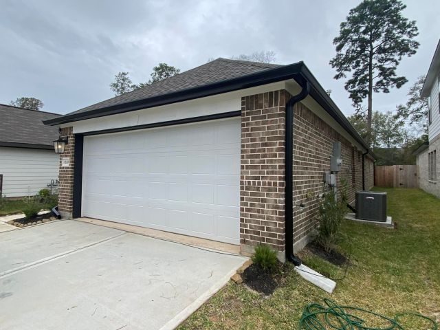 Black seamless gutter and downspout wrapping the garage corner of a brown-brick Conroe home