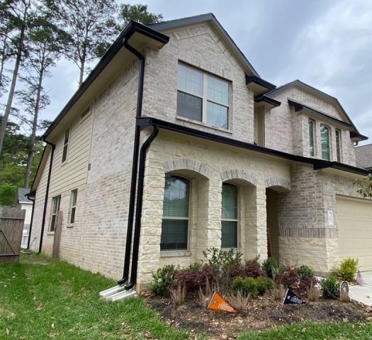 Black seamless gutters and downspouts outlining the two-story light-brick front of a Montgomery home