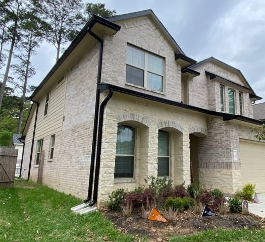 Black seamless gutters and downspouts outlining the two-story light-brick front of a Montgomery home