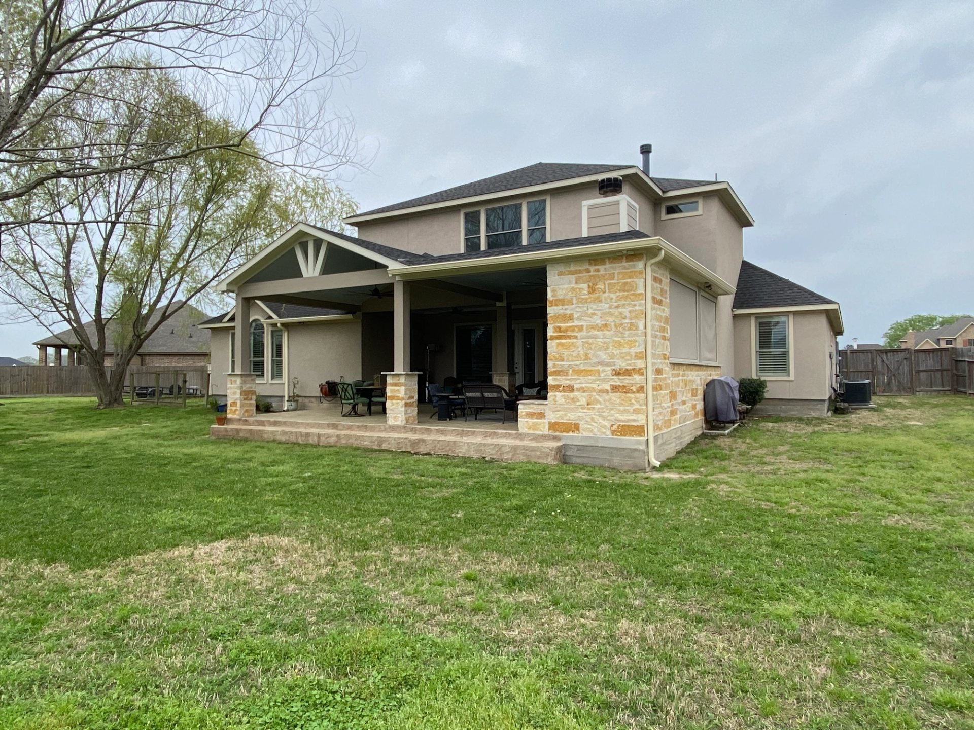 Wide backyard view of beige seamless gutters and matching downspouts around a stone-and-stucco covered patio in Montgomery