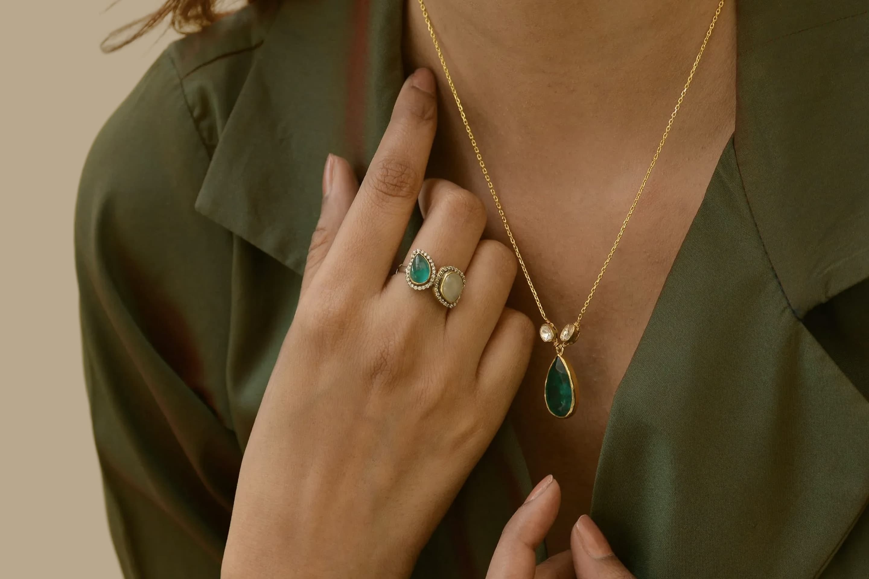 Model wearing a gold necklace with a green teardrop gemstone pendant and matching green gemstone ring.