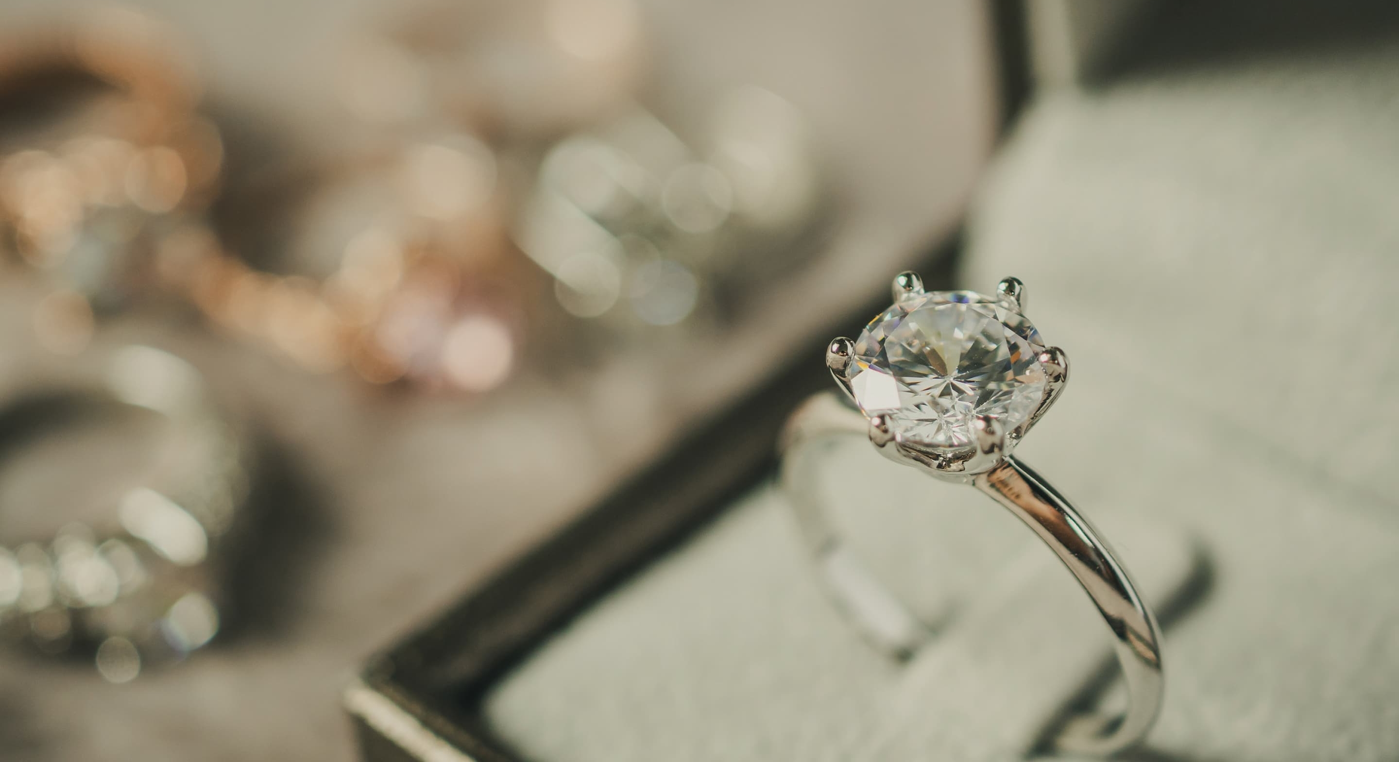 Diamond engagement ring inside ring box with other rings in the distance blurred by depth of field.
