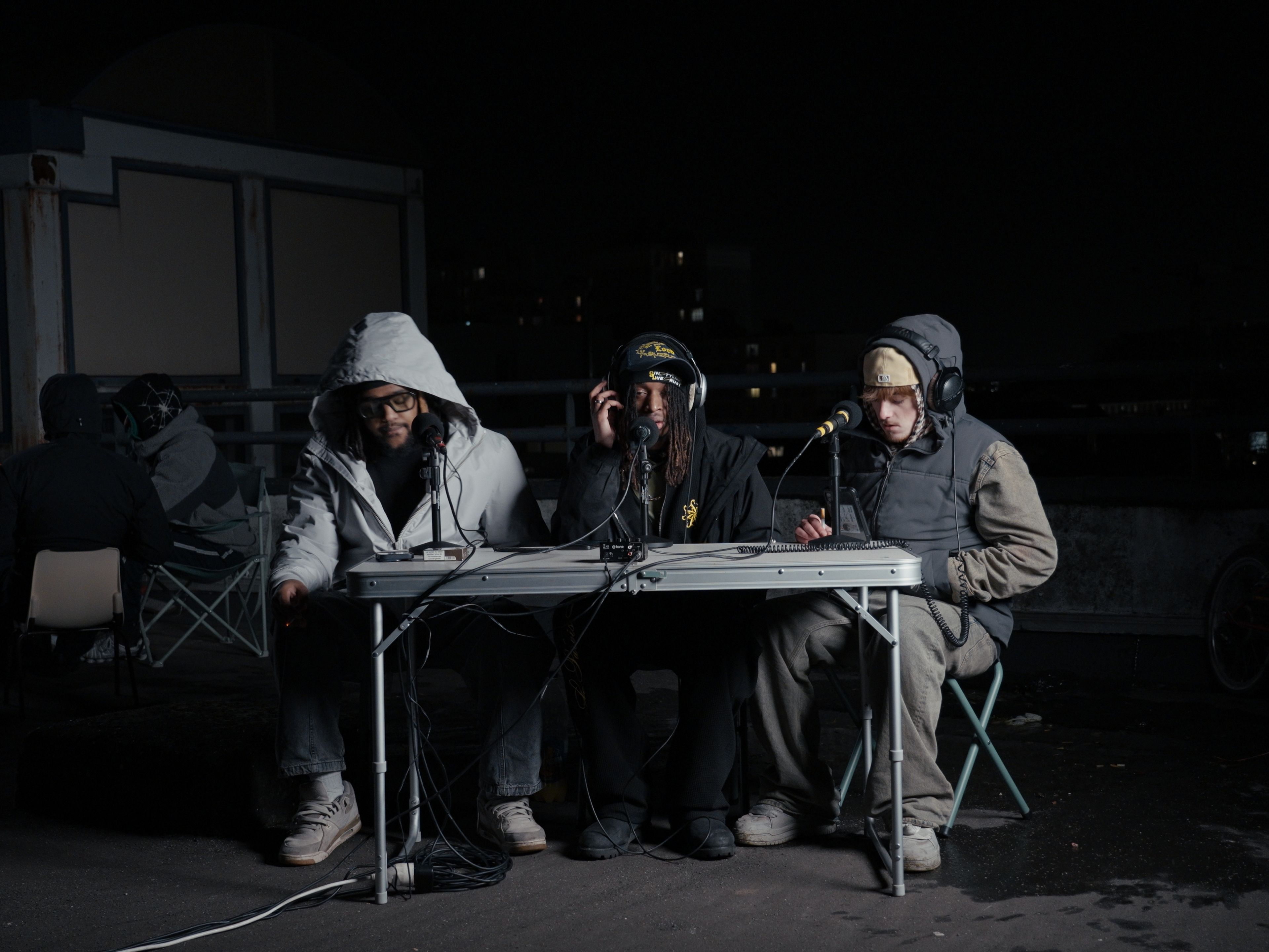 plan moyen des 3 artistes assis face à une table avec leur micro