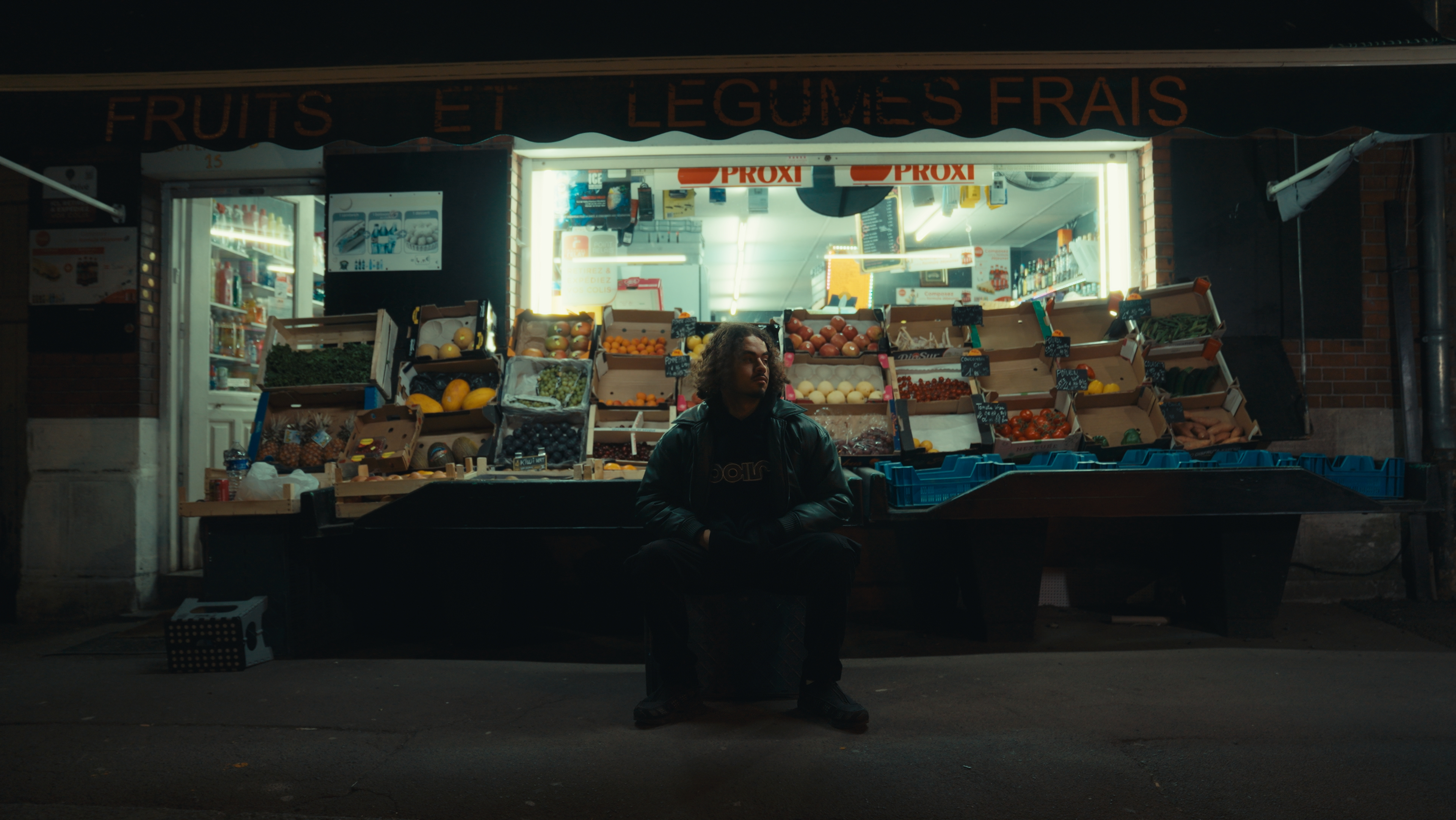 L'artiste est assis devant une épicerie et un étal de fruit