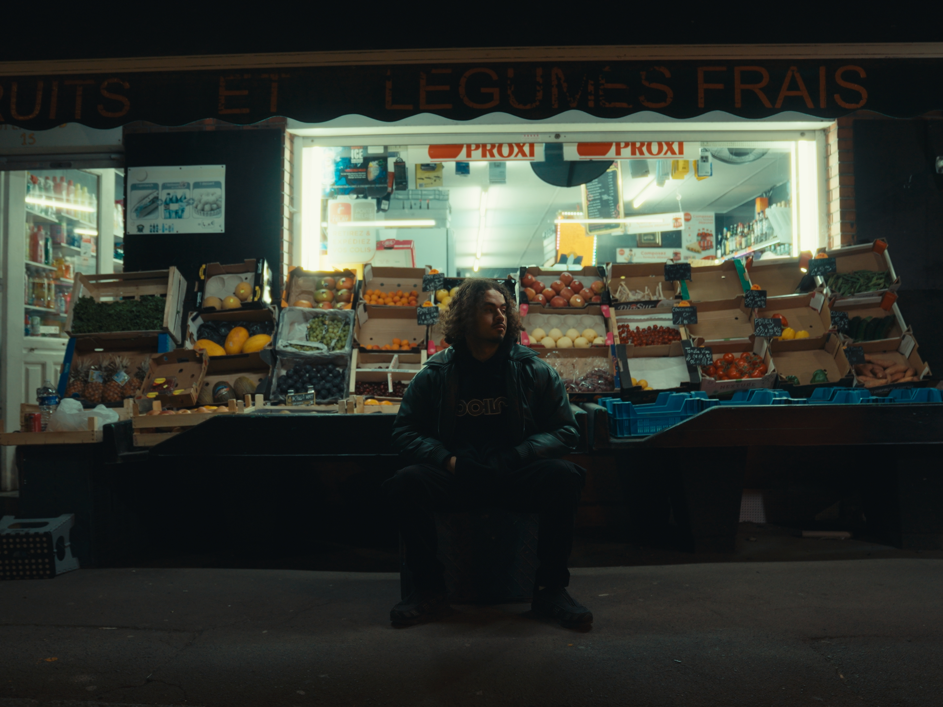 L'artiste est assis devant une épicerie et un étal de fruit