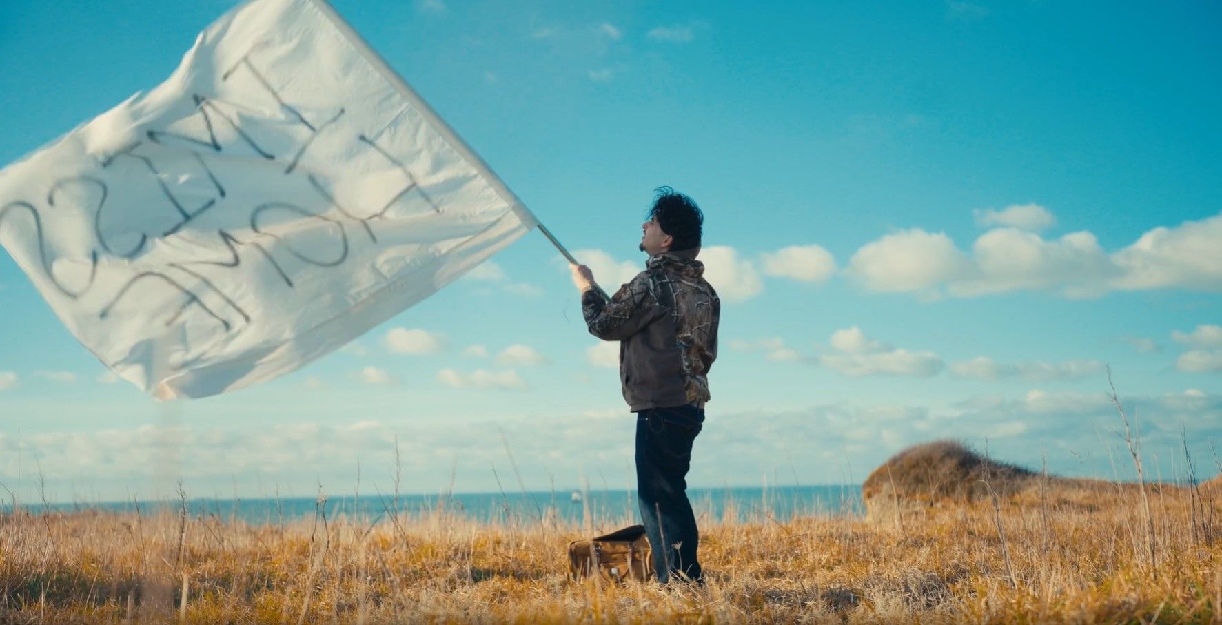 plan large de l'artiste face à la mer qui brandit un drapeau
