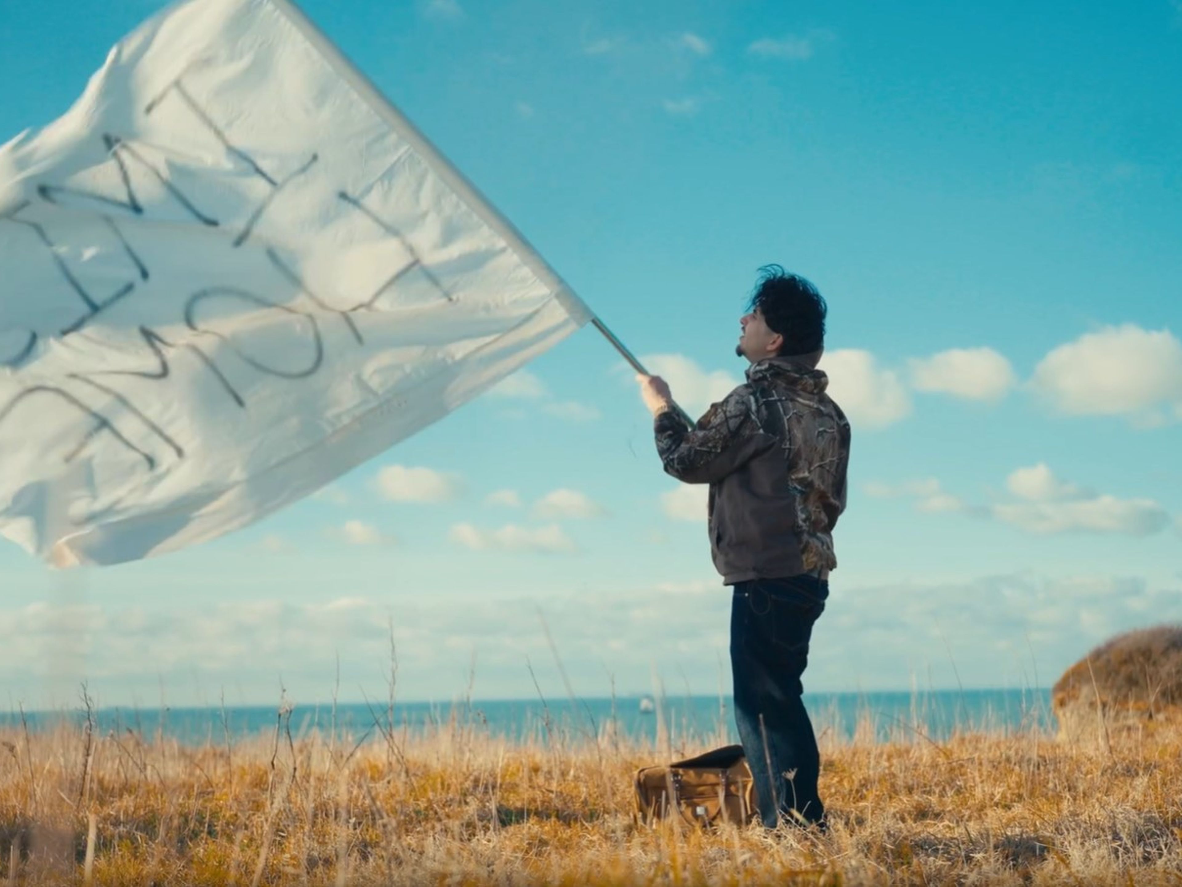 plan large de l'artiste face à la mer qui brandit un drapeau