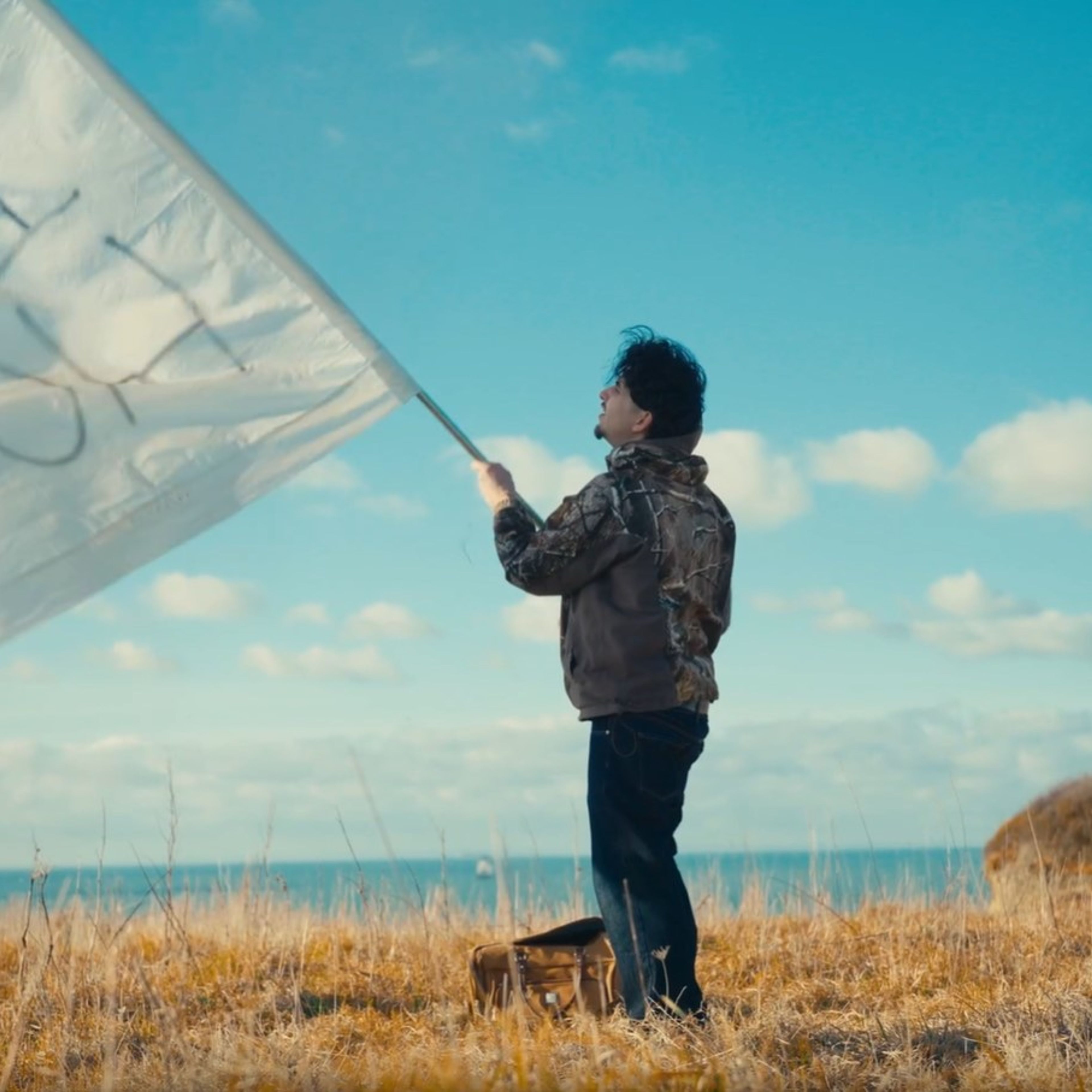 plan large de l'artiste face à la mer qui brandit un drapeau