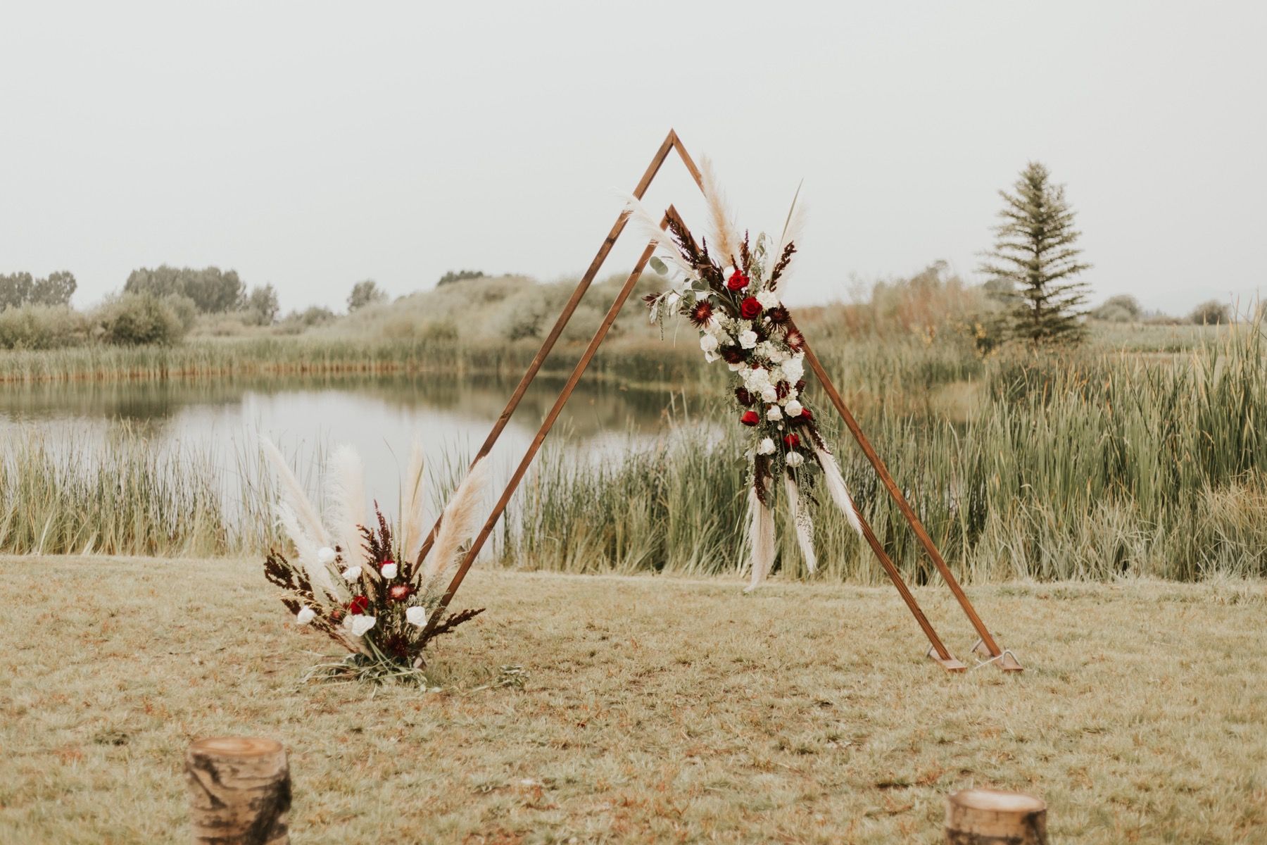 Wooden A-frame wedding arch with florals beside the lodge pond