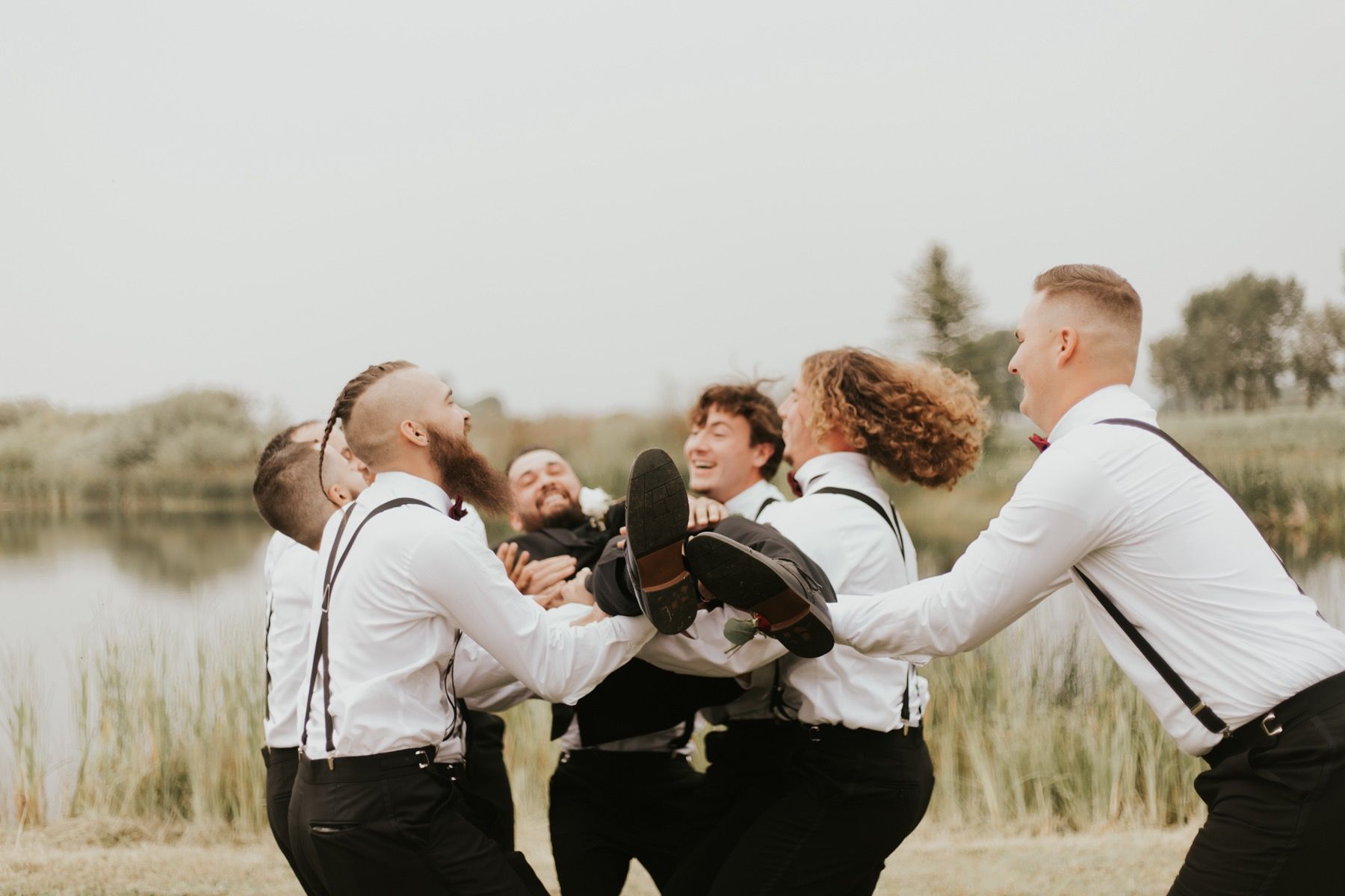Groomsmen in white shirts and suspenders lifting the groom
