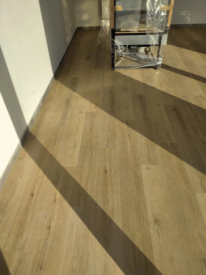 Drugi pokój po ułożeniu paneli — ciepły brąz drewna, meble zabezpieczone folią