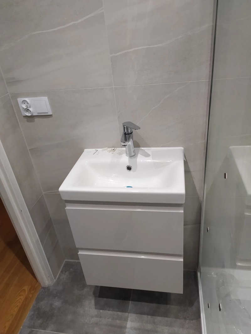 Strefa umywalki z białą szafką podblatową, chromowaną baterią i szarymi marmurkowymi płytkami