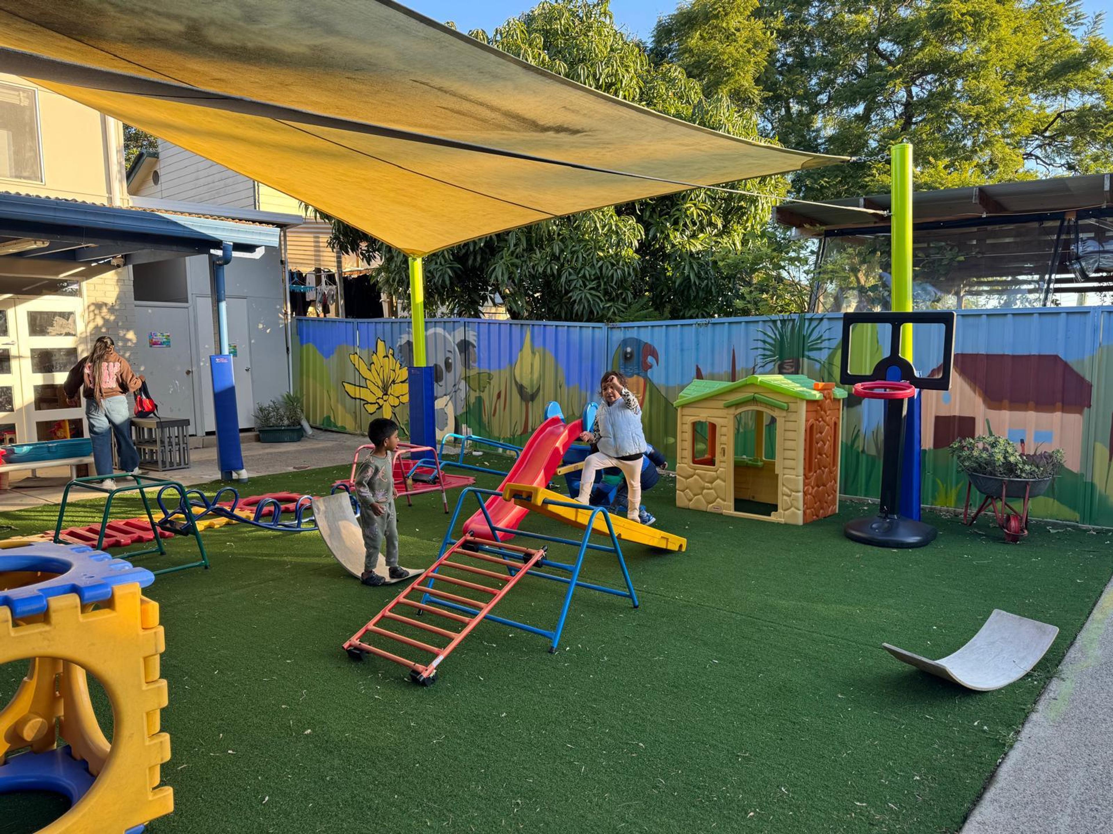 Outdoor play area at our daycare centre in Seven Hills featuring children enjoying slides, climbing structures, and playhouses under shaded supervision.