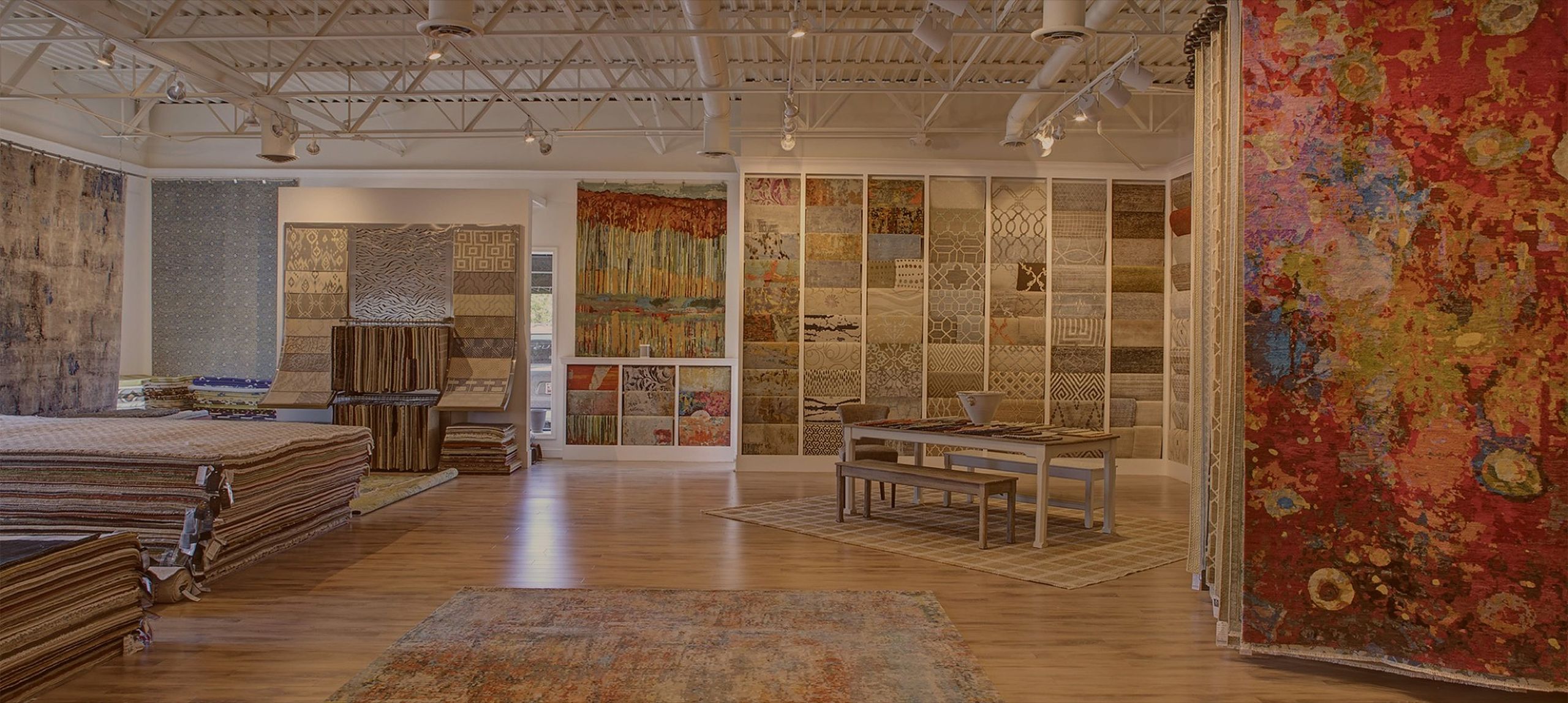 The Senneh Knot showroom: a wall of rug samples, a sample table and a large hanging abstract rug in red and gold