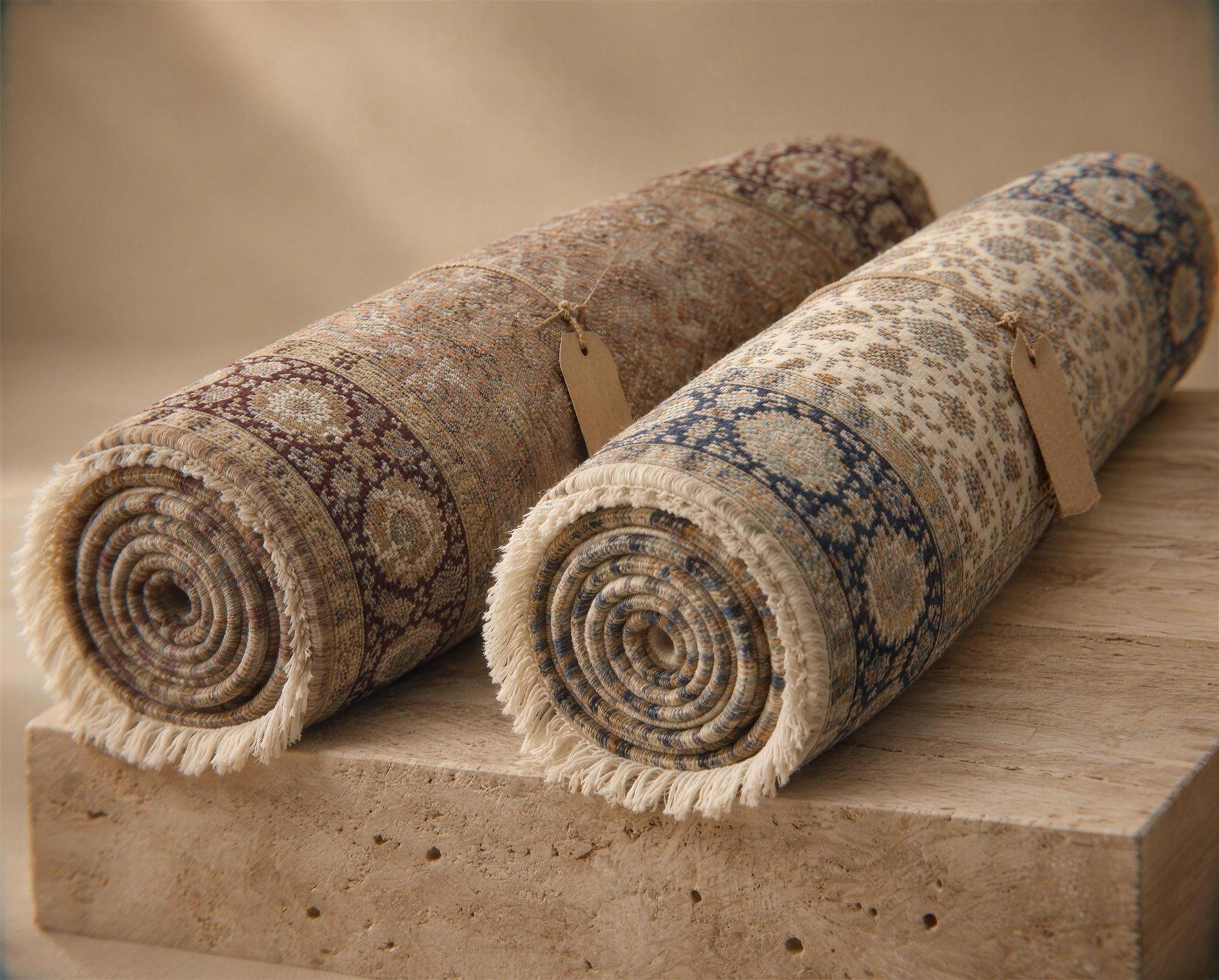 Two rolled hand-knotted rugs in the same Tabriz design, one in taupe and plum, one in ivory and navy, each tied with a paper tag