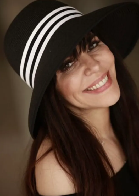 Screenshot+2024-06-13+093409.png Woman smiling and wearing a black hat with white stripes.