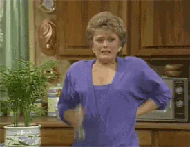 Blanche Devereaux from The Golden Girls fanning herself with a cloth in the kitchen, looking flushed.