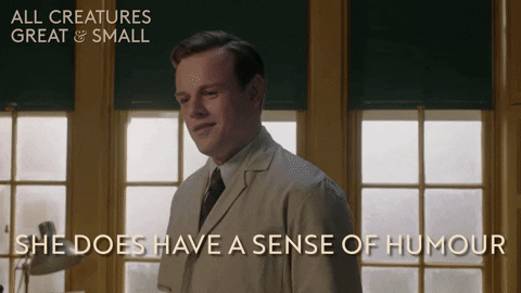 Channel+5+Lol+GIF+by+All+Creatures+Great+And+Small.gif A young man in a beige suit smiles by a window and says 'She does have a sense of humour.'