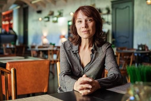 image-01-rId6.png A woman sits with her hands clasped at a table in a warmly lit restaurant.