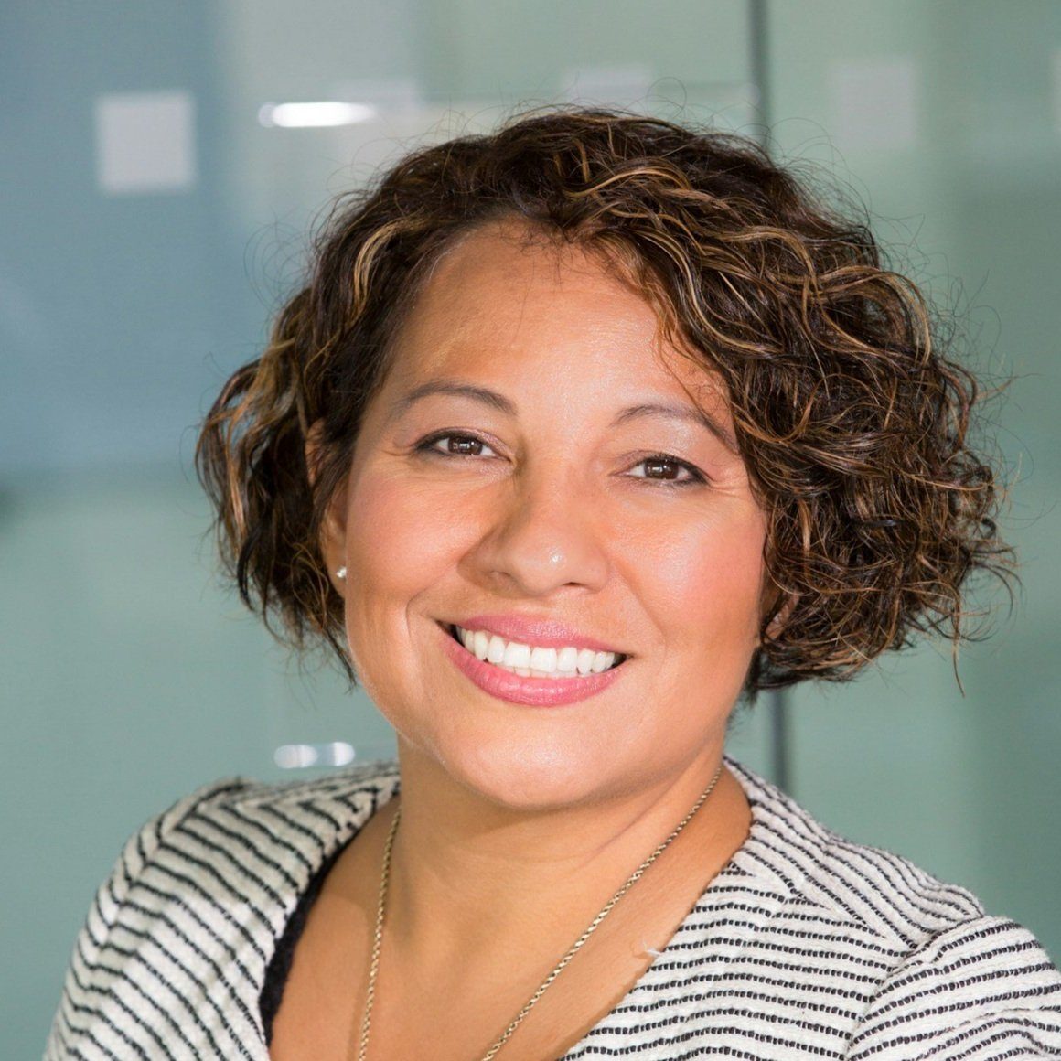image-asset.jpg Smiling woman with curly hair wearing striped blazer in an office setting