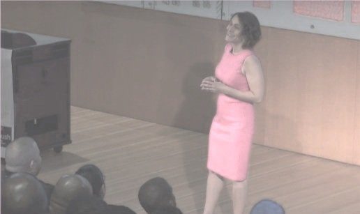 A woman in a pink dress speaking on stage to an audience
