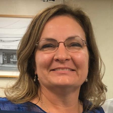 A woman with glasses smiling in an indoor setting.