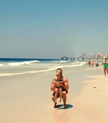 72f37329-e3ad-bf10-f0e7-616db01a7bfd.gif A man tosses a young girl into the air and catches her on a sunny beach.