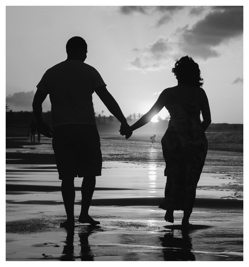 Silhouette of a couple holding hands while walking on a beach at sunset.