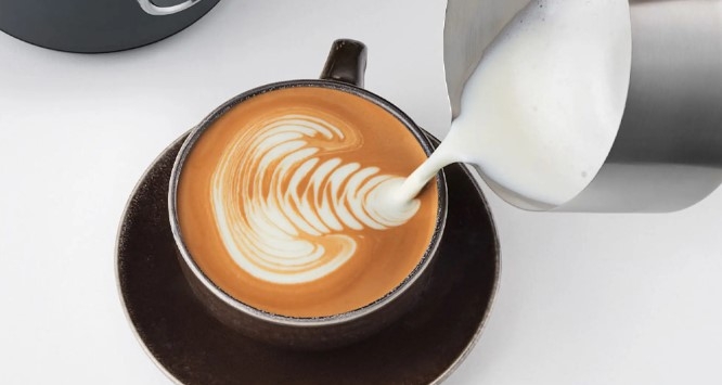 Mjölkskummare, skummad mjölk som hälls upp i kaffe i kopp och skapar ett fint mönster
