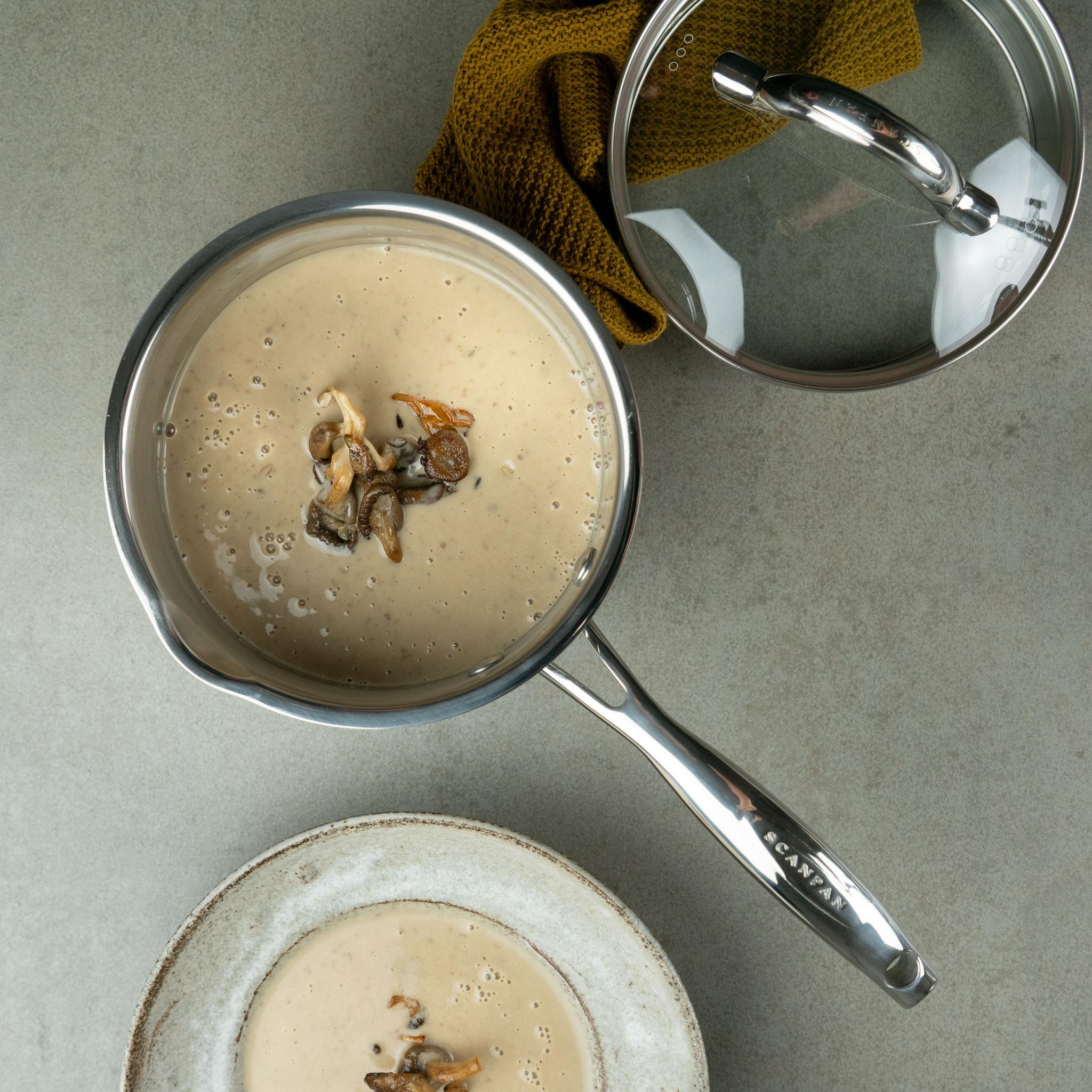 Kattila ja kulho pöydällä jotka ovat täynnä sienikeittoa