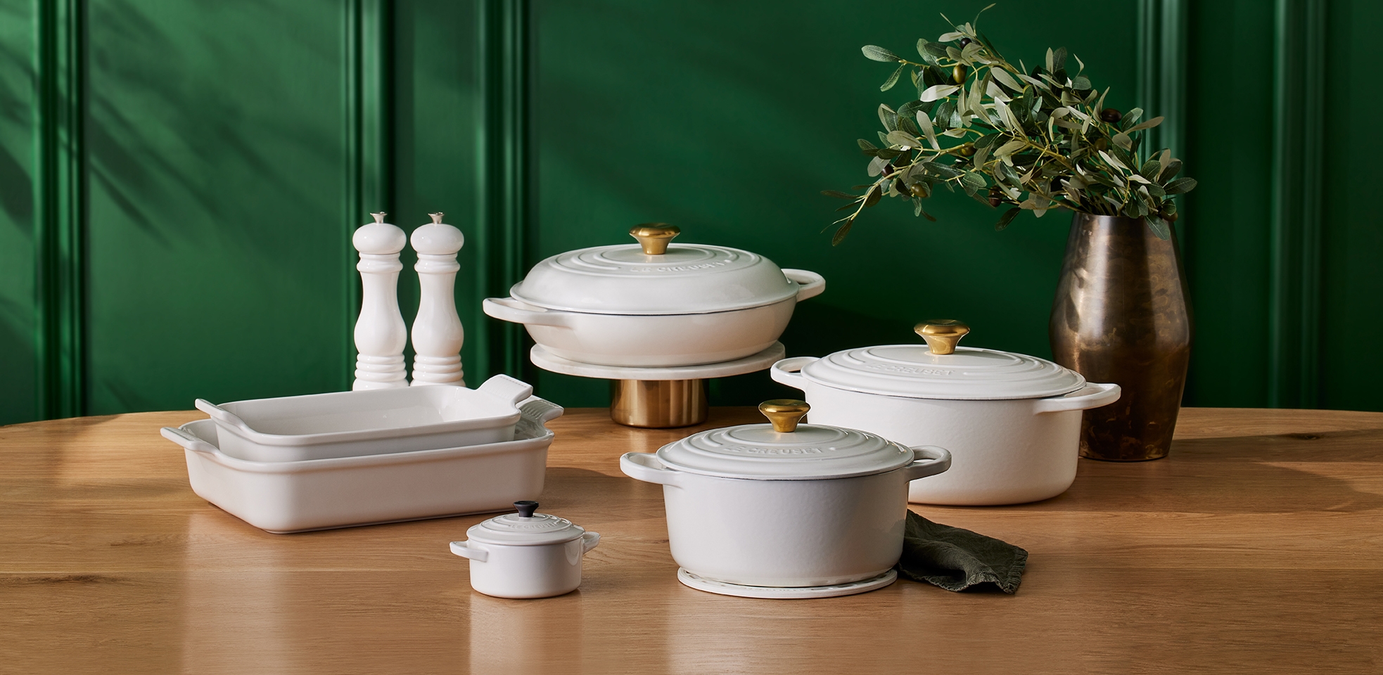 Le Creuset White ovnsformer og gryter i forskjellige størrelser på trebord mot grønn vegg