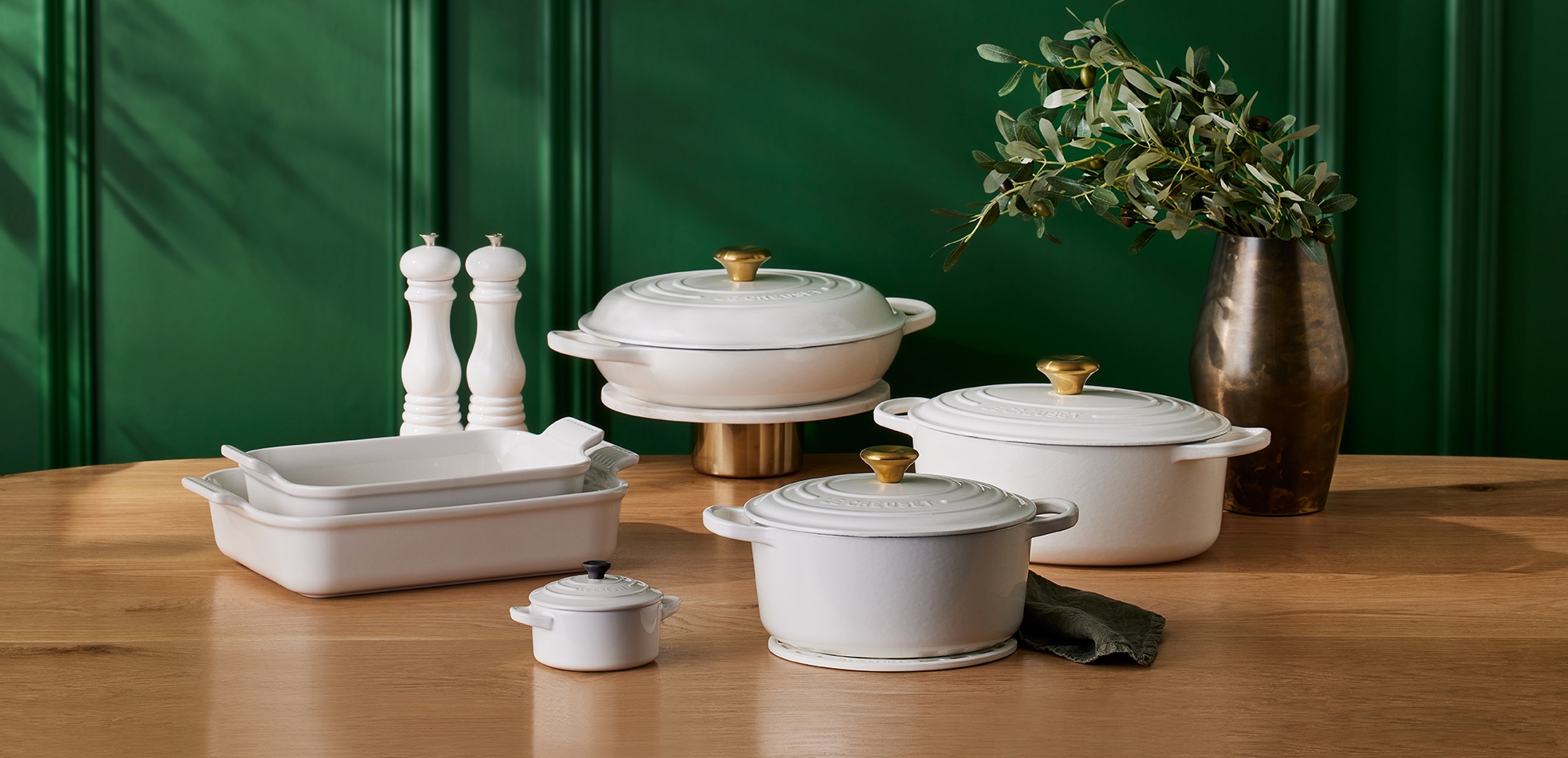Le Creuset White ovnsformer og gryter i forskjellige størrelser på trebord mot grønn vegg