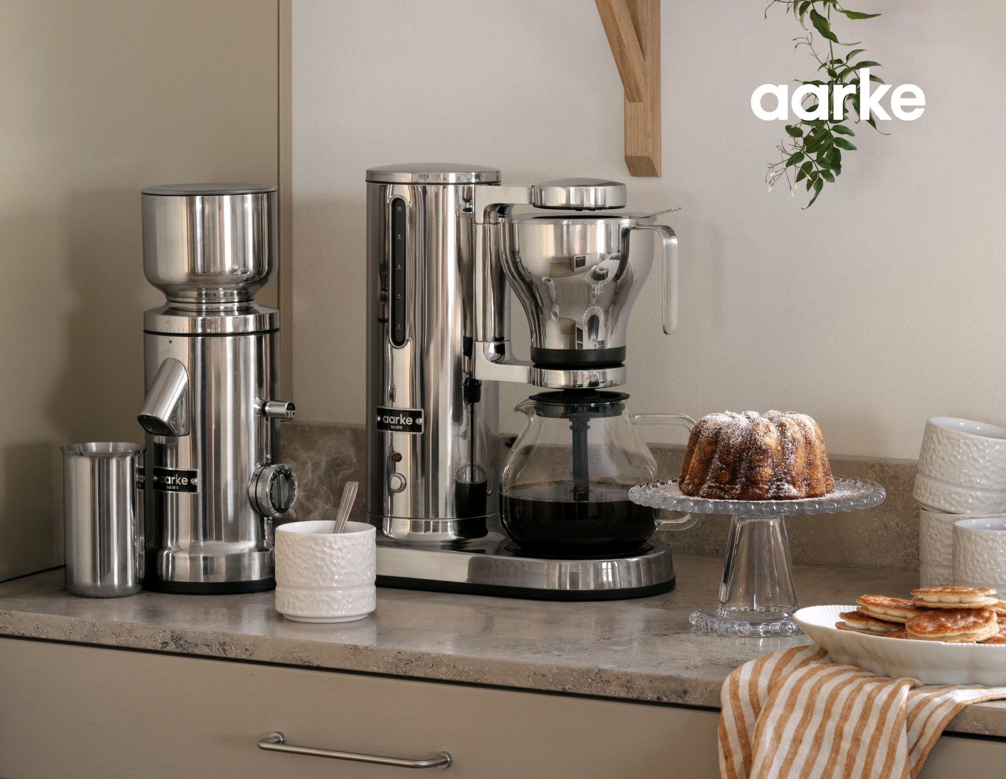 Aarke coffee grinder and coffee maker on a kitchen counter with a bundt cake and pancakes.