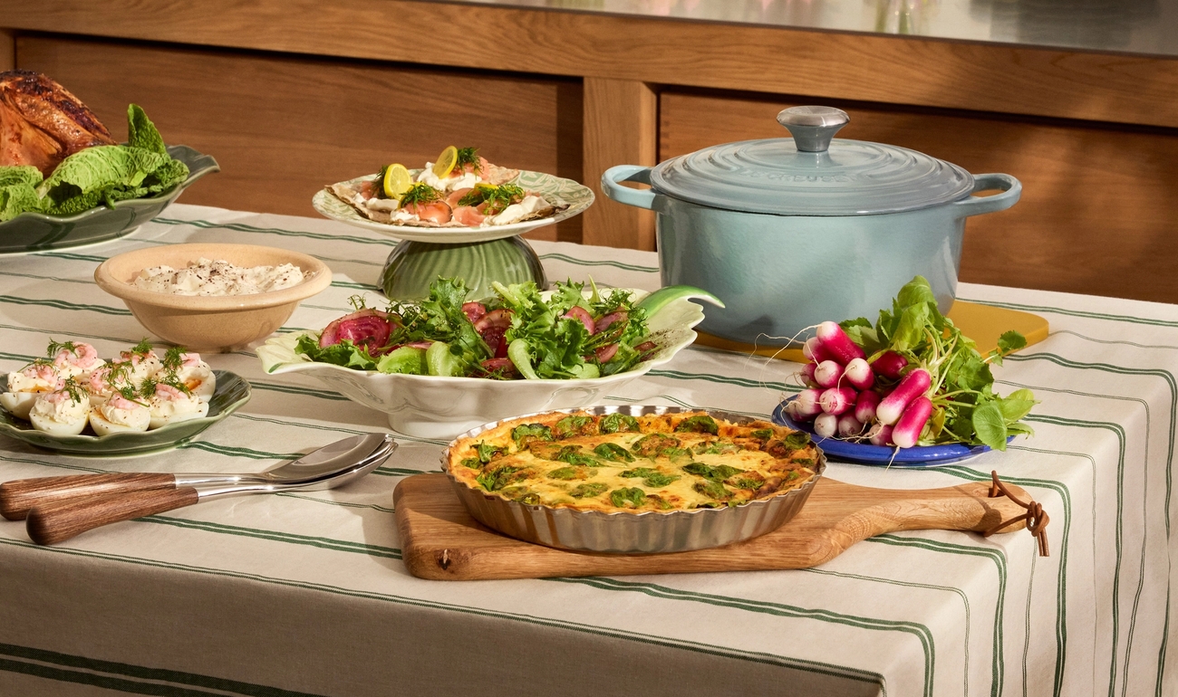 Et festlig måltid servert på en stripete duk og på en kjøkkenbenk, med pai, salater, brød, kake og vårdekorasjoner.