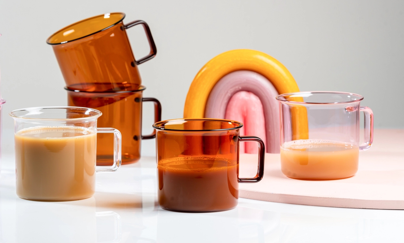 värilliset Muurla lasimukit, osa täytetty juomilla, aseteltuna pastellinsävyisen sateenkaarikoristeen kanssa