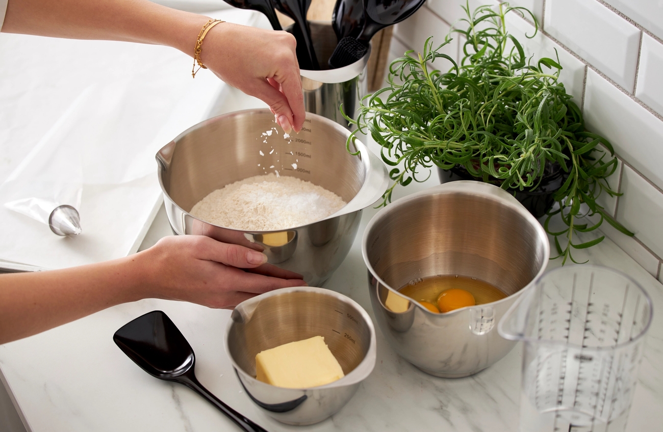 En person häller mjöl i en metallskål på en bänkskiva.