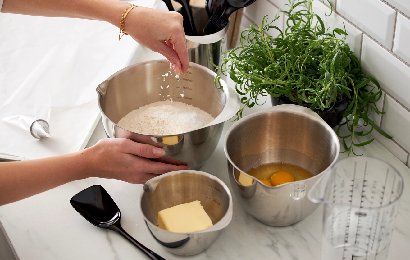 En person häller mjöl i en metallskål på en bänkskiva.