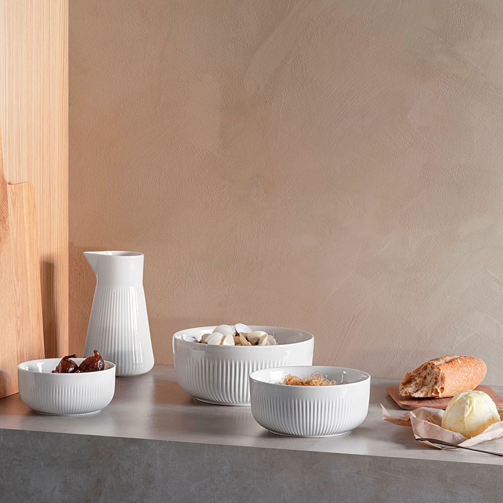 Valkoisia uurrettuja kulhoja, joissa on viikunoita, simpukoita ja kuivattuja nuudeleita, sekä valkoinen maljakko.