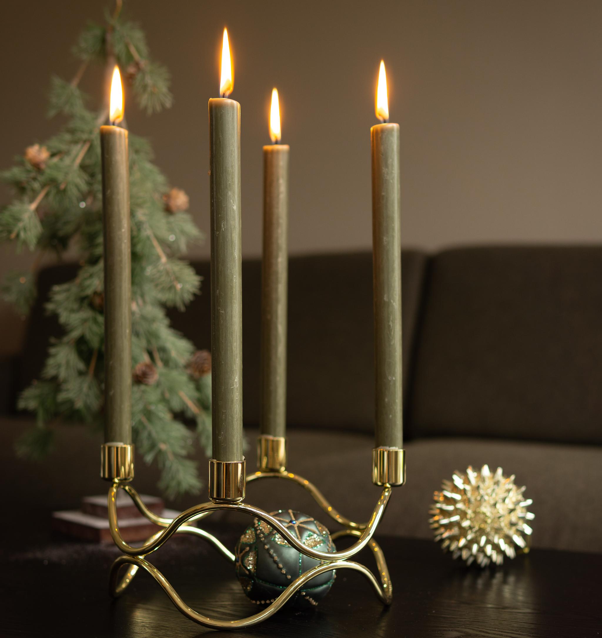 Kultainen kynttelikkö, jossa palaa neljä vihreää kynttilää, taustalla sumeita joulukoristeita.