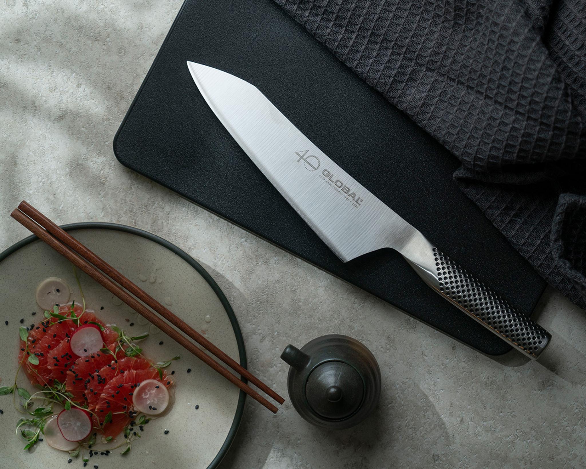 Global-kockkniv på svart skärbräda bredvid sashimi, ätpinnar och en liten tekanna.