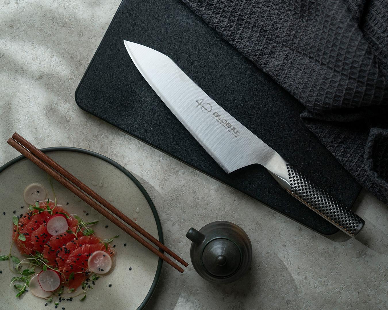Global-kockkniv på svart skärbräda bredvid sashimi, ätpinnar och en liten tekanna.