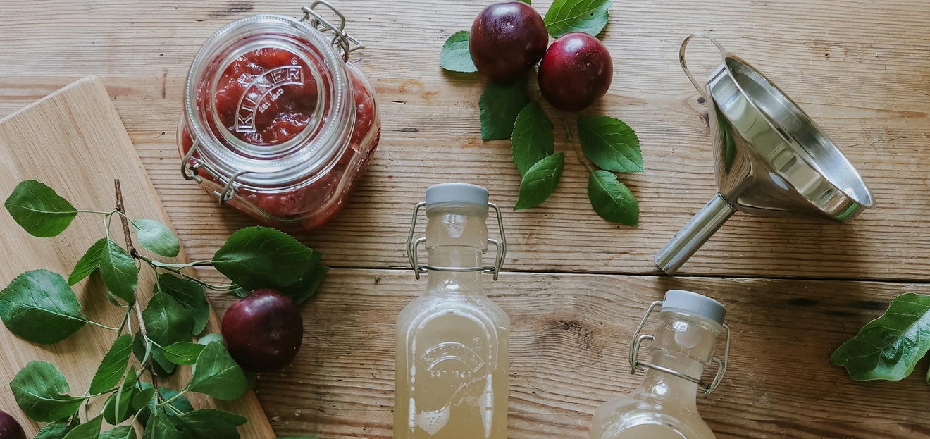 Valmista oma hillo ja mehu - Lasipullot ja lasipurkit omenien ja lehtien kera puisella pöydällä